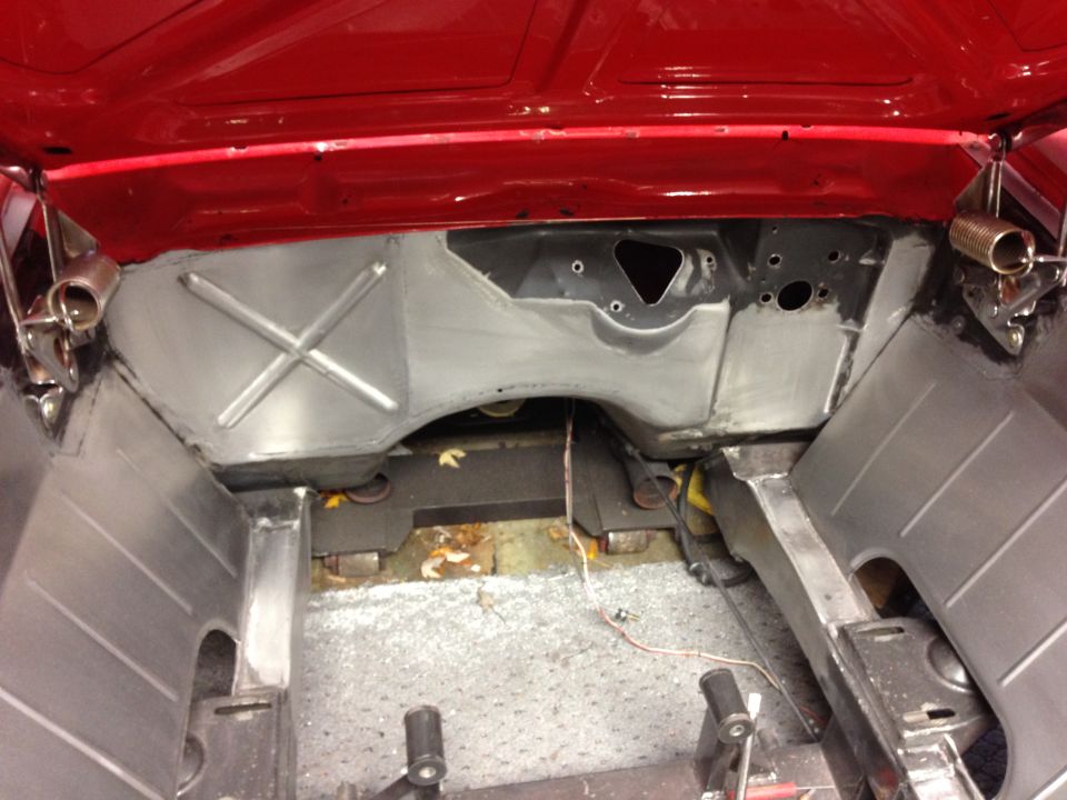 Interior of a red classic car with firewall and floor exposed during restoration.
