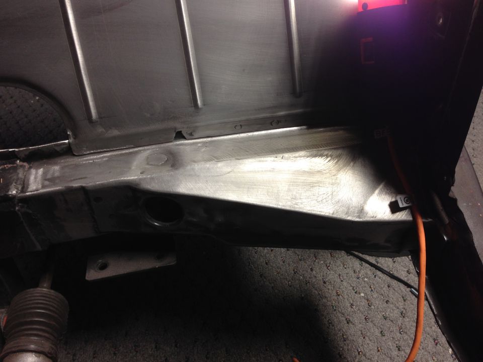 Underside of a vehicle chassis with metal work and an orange cable.