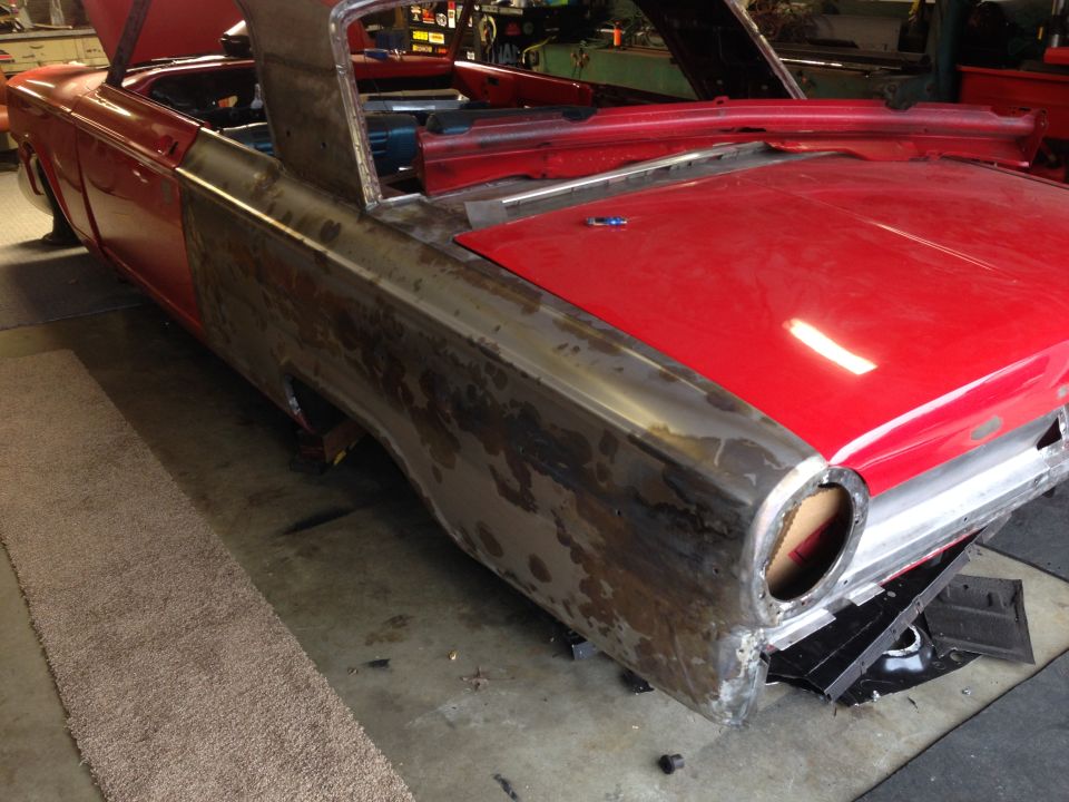 Red classic car undergoing restoration, showing bare metal rear quarter panel with rust.