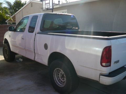 1988 Ford Bronco - A white four-door pickup truck is parked on a concrete driveway in front of a house. The truck has aftermarket wheels and appears to be lif…