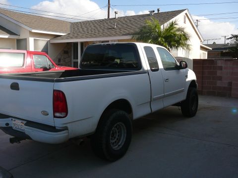 1988 Ford Bronco - A white Ford F-150 pickup truck is parked in a driveway in front of a house. The truck is viewed from the rear passenger side, showing its…