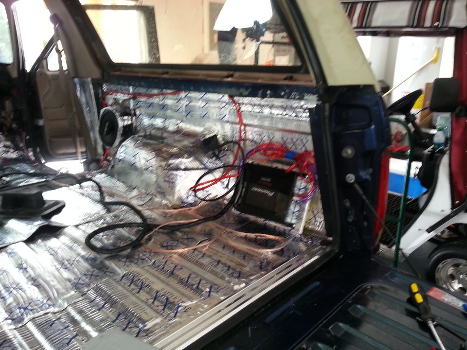 Interior of a vehicle with soundproofing material on the floor and doors, and wiring for an audio system. A Pioneer amplifier is visible