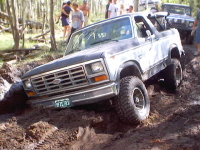 1983 Ford Bronco - This 1983 Ford Bronco is stuck deep in the mud, with onlookers present.