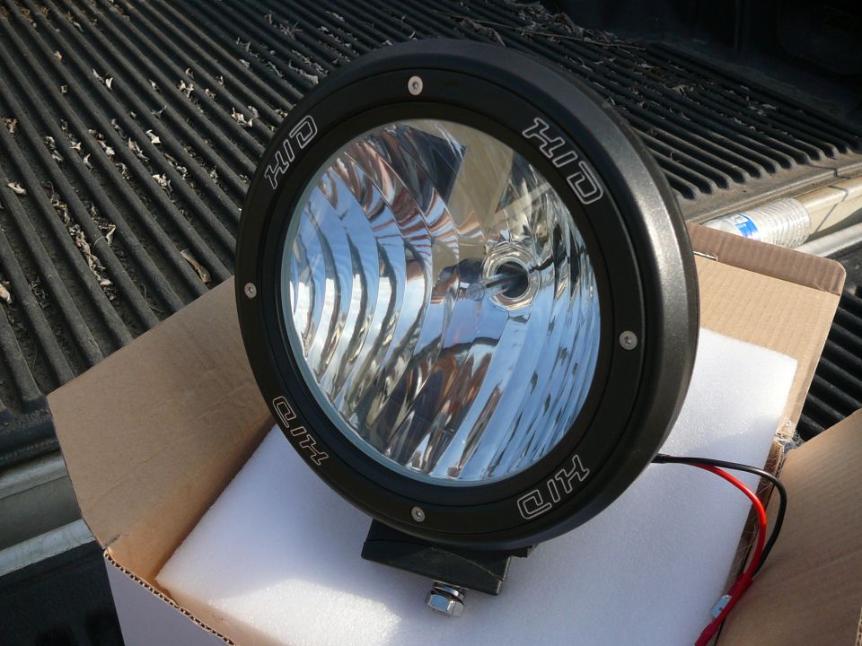 Black HID off-road light with 'HID' text on the bezel, sitting in a cardboard box on a truck bed