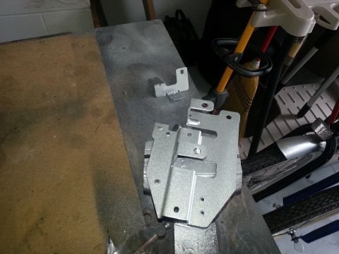1994 Ford Bronco - Several metal brackets are laid out on a workbench, appearing to be prepped for painting or recently painted.