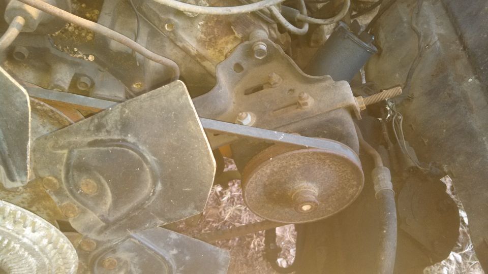 Close-up of an engine's belt and pulley system, showing rust and wear