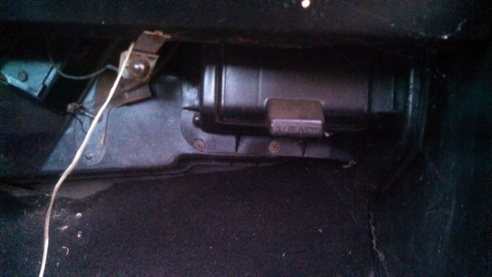 Close-up of a black plastic automotive component with a metal bracket and white wire.