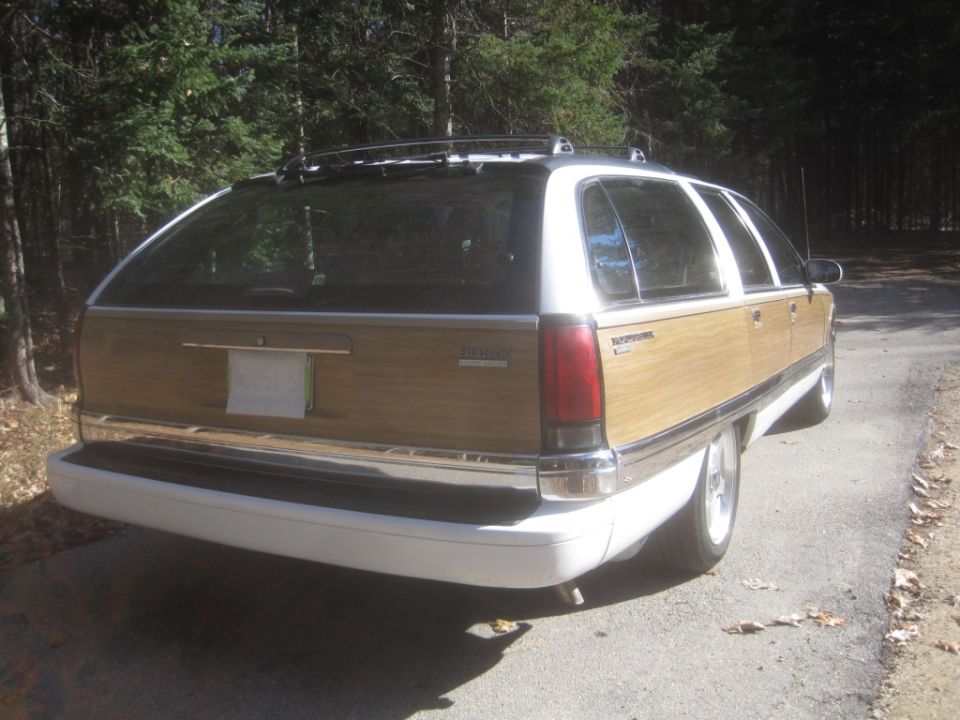 White and wood-paneled station wagon parked on a road next to a forest.