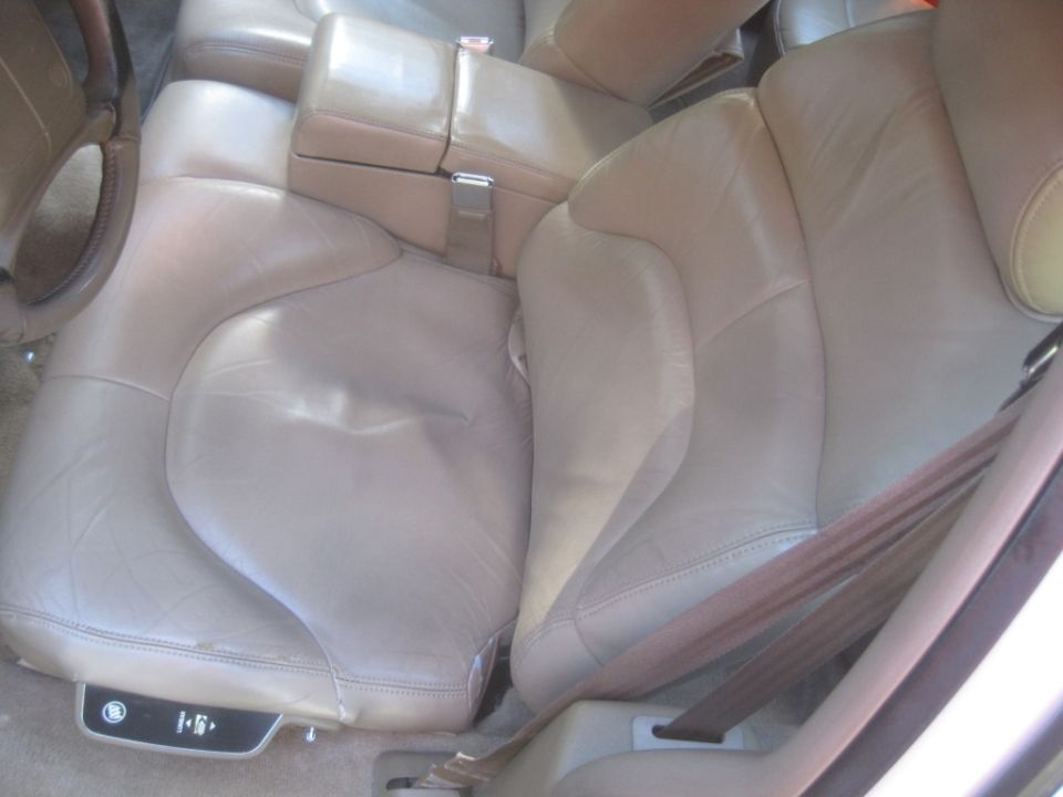 Tan leather car seat interior with steering wheel and armrest.