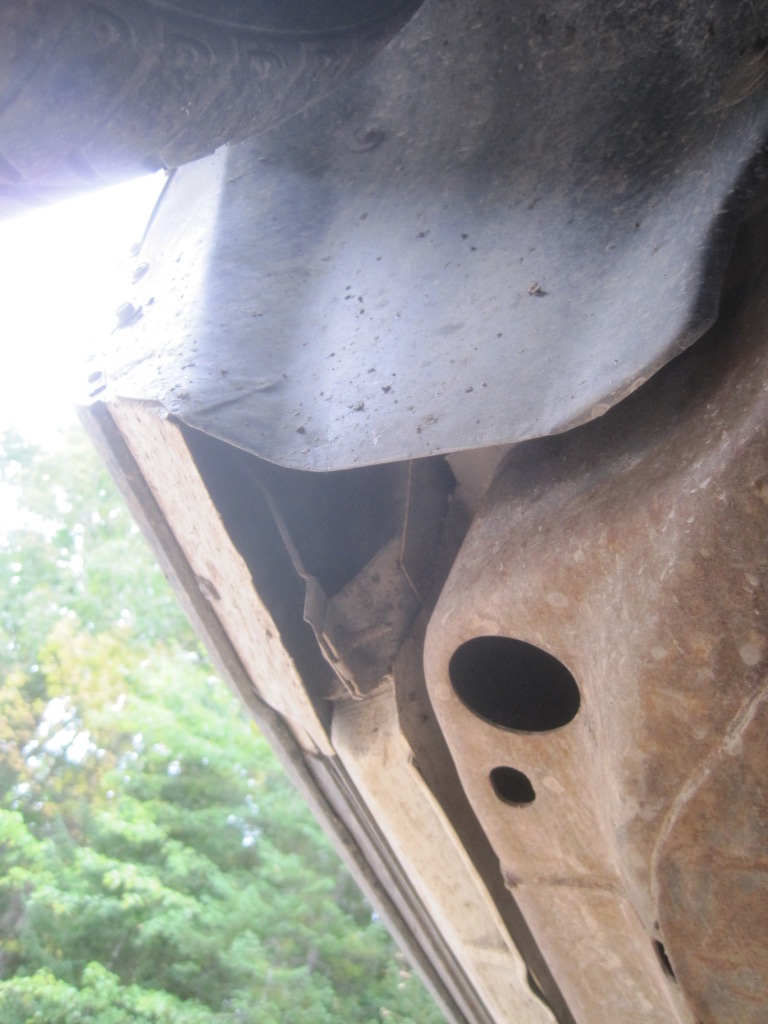 Underside of a vehicle showing wheel well, rusty frame, and splash guard.