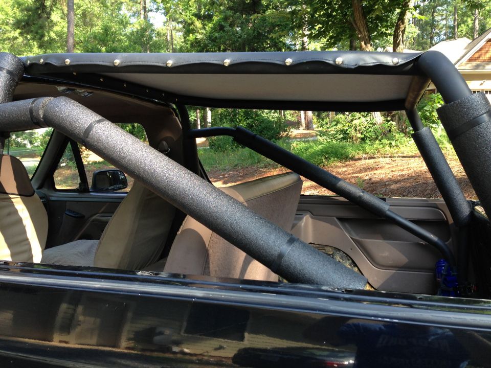 Interior view of a black 1993 Ford Bronco with a roll cage and tan seats.