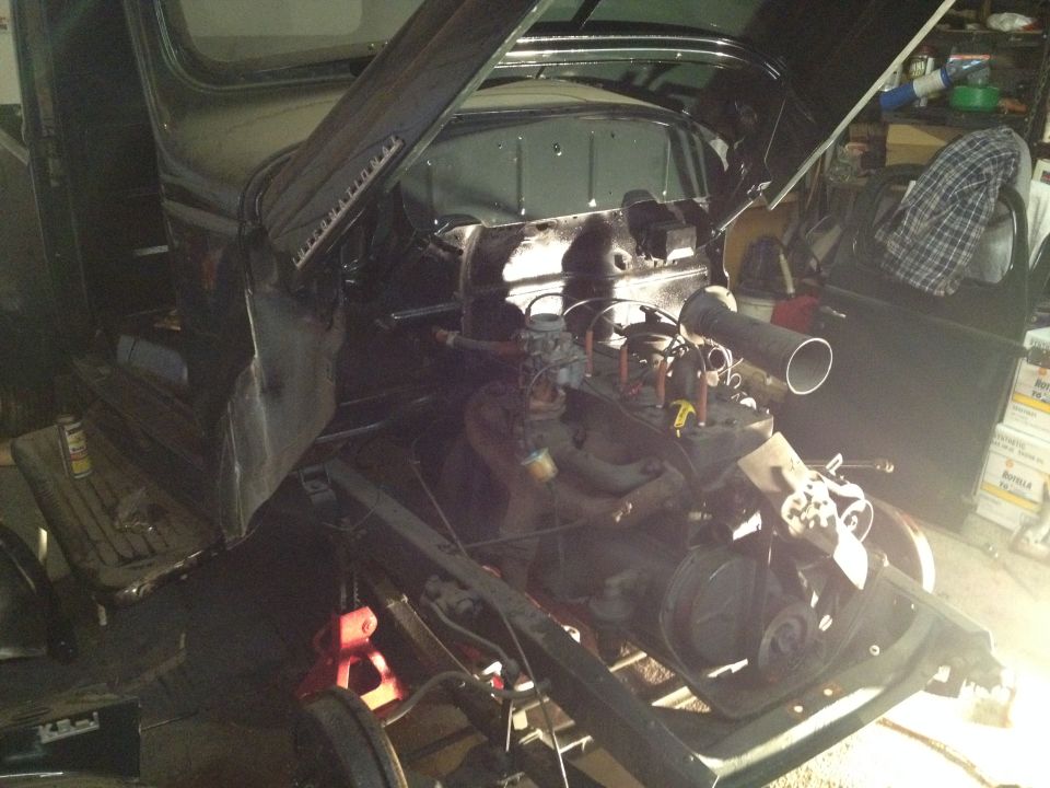 Engine bay of a dark colored vintage truck or SUV undergoing restoration.