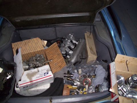 1995 Ford Probe - The open trunk of a blue car is filled with automotive parts, including engine components, boxes, and packaging. Several cardboard boxes ar…