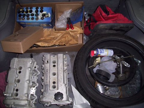 1995 Ford Probe - A collection of engine parts, including two cylinder heads, a tire with a spray can and tools inside, and a red tool bag, are organized in…