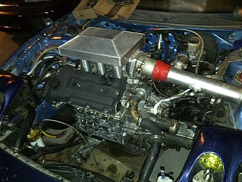 1995 Ford Probe - The engine bay of a blue vehicle, likely a 1995 Ford Probe, is shown with a custom turbocharger setup. The engine features a large intercoo…
