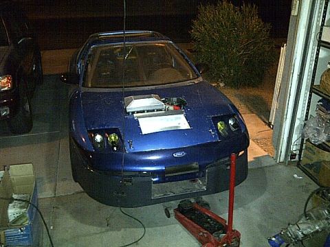 1995 Ford Probe - A modified, dark blue Ford Probe is parked in a garage with its hood open, revealing engine components. A red hydraulic jack is positioned…