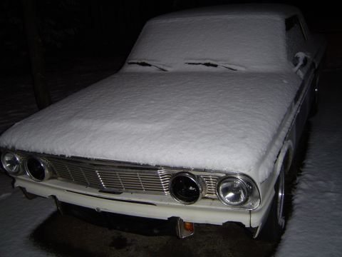 1964 Ford Fairlane - A 1964 Ford Fairlane sits covered in snow, with only its front grille and headlights partially visible.