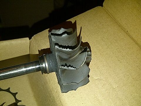1995 Ford Probe - A damaged turbocharger turbine wheel and shaft are shown resting on a cardboard surface. The turbine wheel has several broken and bent blad…