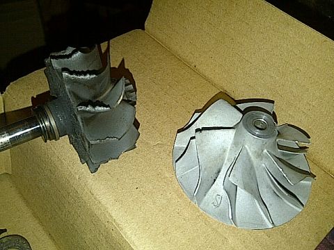1995 Ford Probe - Two turbocharger compressor wheels are shown in a cardboard box. One wheel is severely damaged with broken blades, while the other appears…