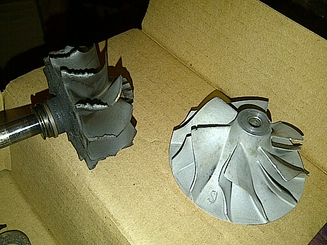 Damaged and intact turbocharger compressor wheels in a cardboard box.