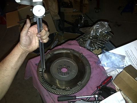1995 Ford Probe - A person's hand holds a caliper over a flywheel, measuring its diameter. The flywheel has a ring gear around its outer edge and is resting…