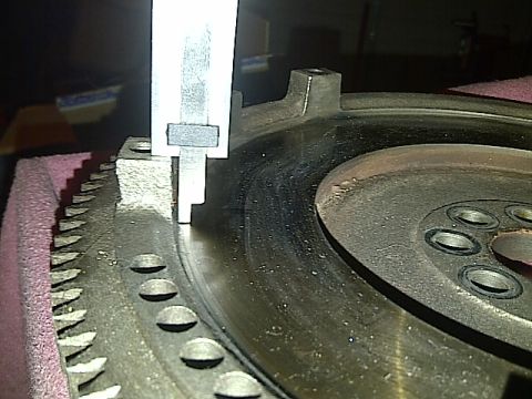 1995 Ford Probe - A close-up view shows a caliper measuring the runout of a metal flywheel with visible teeth around its outer edge. The flywheel is resting…