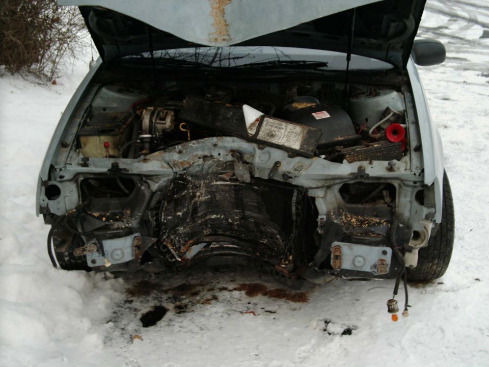 Front of silver car with hood up, burned and stripped front end, sitting in snow