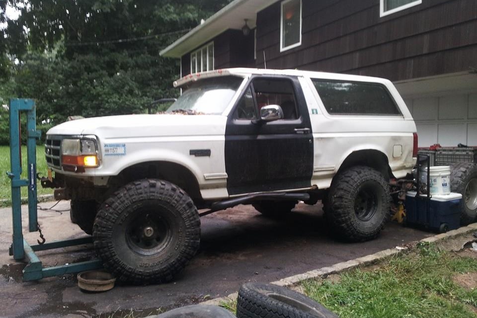 White and black two-door Ford Bronco with large off-road tires in a driveway.
