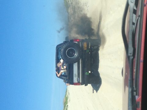 1995 Ford Bronco - A black 1995 Ford Bronco is seen from the rear, kicking up black smoke and dust, with a spare tire mounted on the back.