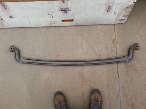 1965 Ford Mustang - A dark gray, curved metal bar with mounting holes at each end is laid out on a concrete surface in front of a cardboard box. The bar appear…
