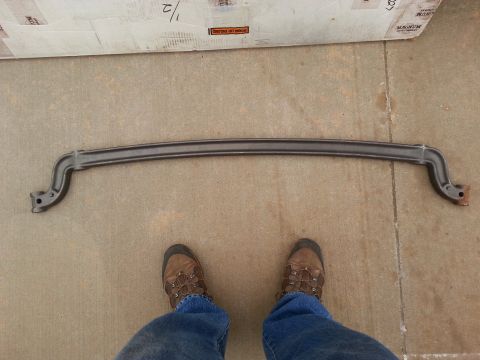 1965 Ford Mustang - A dark gray sway bar is laid out on a concrete surface in front of a cardboard box. The sway bar has mounting brackets with holes at each e…