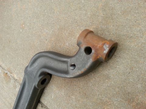1965 Ford Mustang - A close-up, angled view of a dark gray, cast metal automotive part with some rust on one end. The part has two visible holes and a threaded…