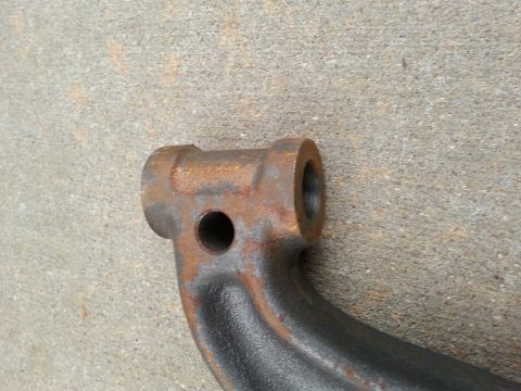 1965 Ford Mustang - A close-up, angled view of a rusty, dark gray metal automotive part, likely a suspension component, resting on a concrete surface.