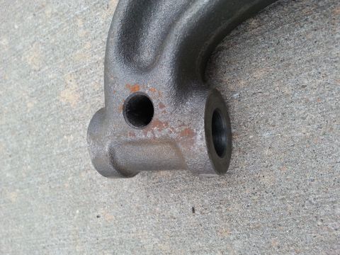 1965 Ford Mustang - A close-up, angled view of a dark gray, cast metal automotive part with a small hole and some rust spots, resting on a concrete surface.
