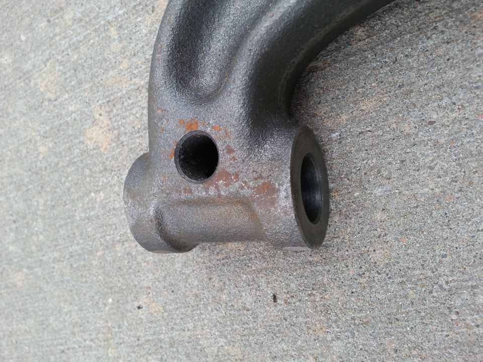 Close-up of a dark gray cast metal automotive part with a hole and rust on concrete.