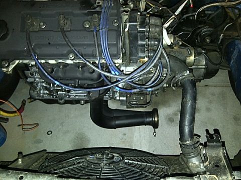 1995 Ford Probe - A close-up, overhead view of a vehicle's engine bay, focusing on the engine block, spark plug wires, and intake piping. A large cooling fan…