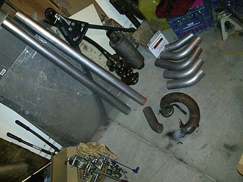 1995 Ford Probe - A collection of exhaust pipes and automotive parts are laid out on a concrete floor. The parts include several bent exhaust tubes, a muffle…