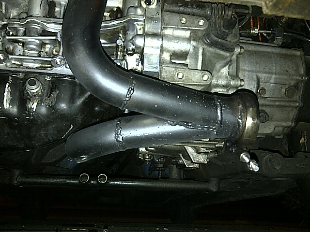 Close-up of custom exhaust manifold and transmission on a vehicle.