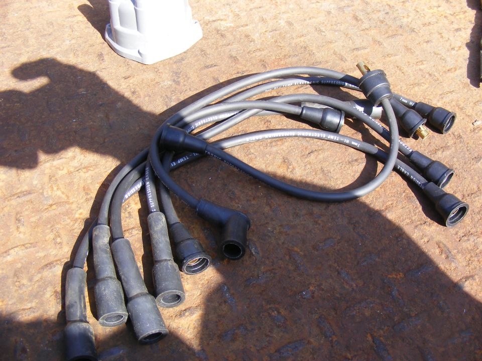 Black spark plug wires and a white distributor cap on a rusty surface.