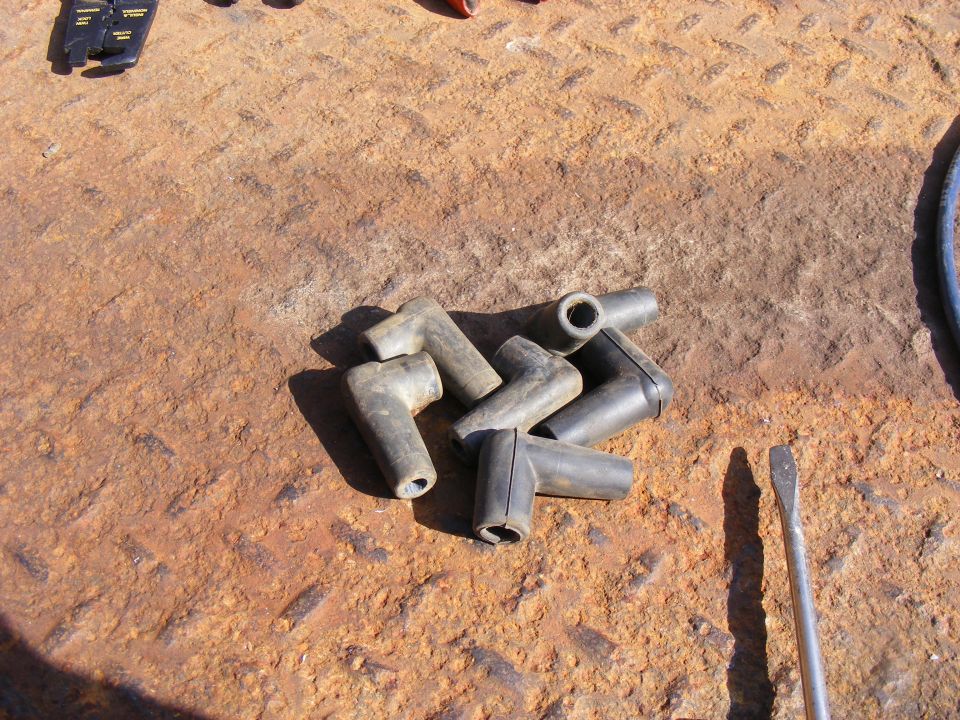 Black spark plug wire boots and screwdrivers on a rusty metal surface.