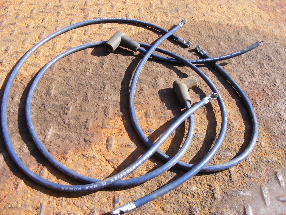 Blue spark plug wires with black boots on a rusty metal surface.