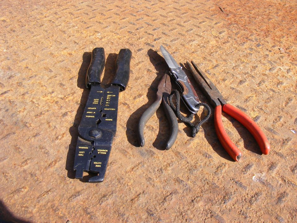 Wire strippers, pliers, and a pocket knife on a rusty surface.