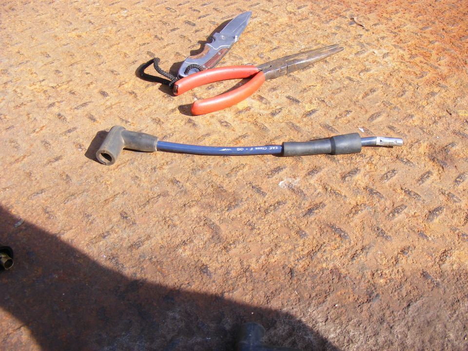 Spark plug wire on rusty metal surface with pliers and pocket knife