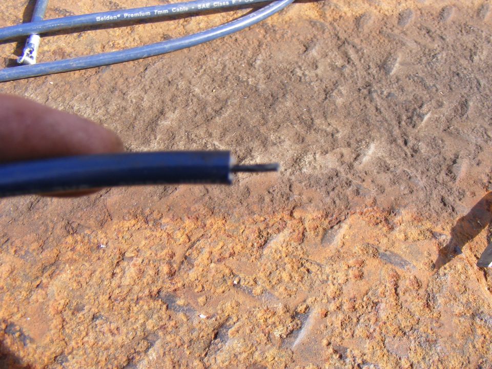 Close-up of a blue wire with exposed copper conductor on a rusty surface.