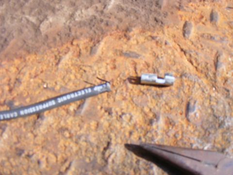 Damaged electronic suppression cable on a rusty surface with pliers.