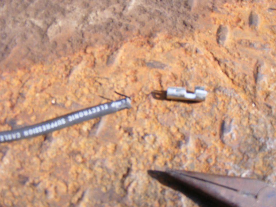 Damaged electronic suppression cable on a rusty surface with pliers.