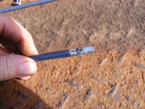 Damaged blue cable with metal connector on rusty surface