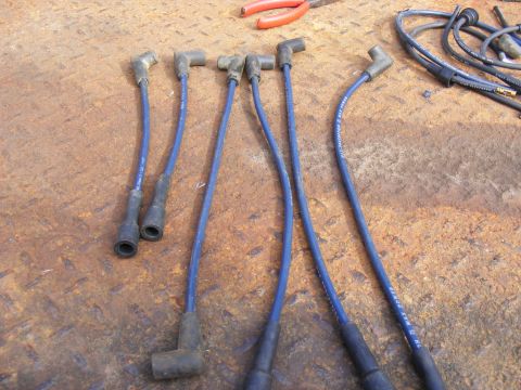 Blue spark plug wires with black boots on a rusty metal surface.