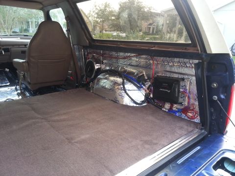 1994 Ford Bronco - Photograph of an SUV cargo area with subwoofer, amplifier, and audio wiring over sound-deadening, not a technical document.