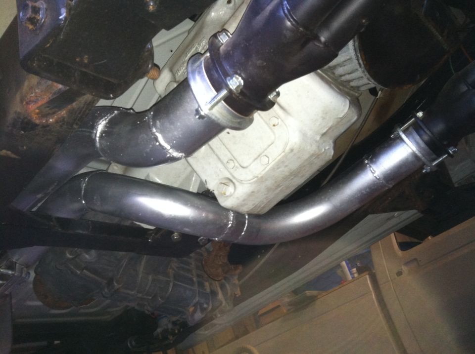Underbody shot of welded dual exhaust pipes with band clamps beneath a vehicle's oil pan and transmission